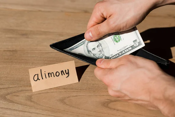 Vue recadrée de l'homme tenant un portefeuille et un billet en dollar près du papier avec lettrage de pension alimentaire — Photo de stock