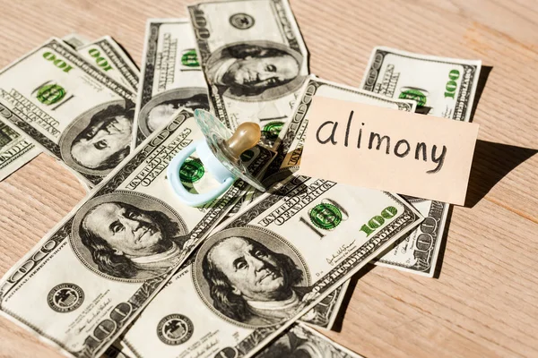 Baby nipple on dollar banknotes near paper with alimony lettering — Stock Photo