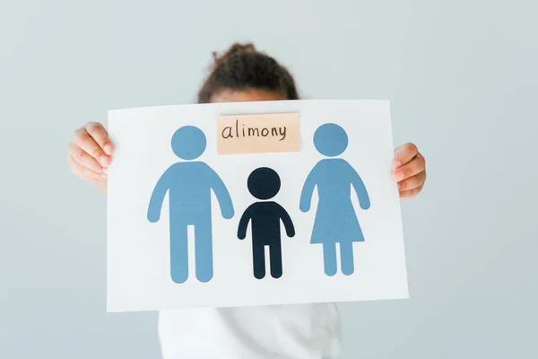 Afro-américain enfant couvrant visage tout en tenant du papier avec la famille dessinée et lettrage de pension alimentaire isolé sur blanc — Photo de stock