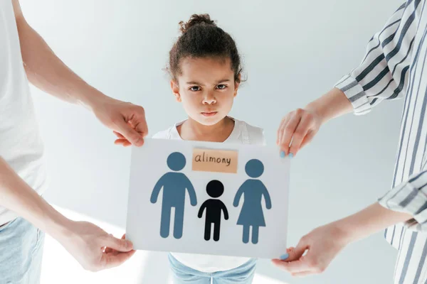 Enfoque selectivo de los padres sosteniendo papel con letras dibujadas de la familia y de la pensión alimenticia cerca del niño afroamericano adoptado en blanco - foto de stock