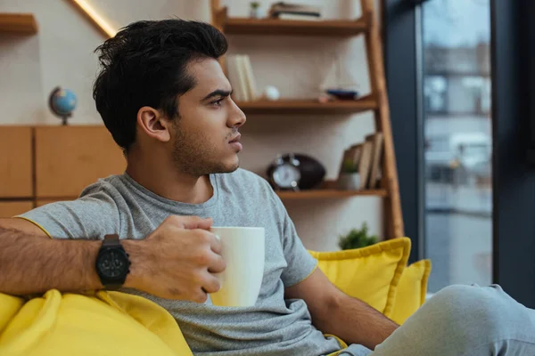 Nachdenklicher Mann hält Tasse Tee auf Sofa im Wohnzimmer — Stockfoto