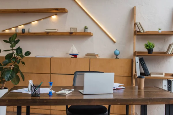 Tisch mit Laptop, Sanduhr und Stifthalter im Büro — Stockfoto