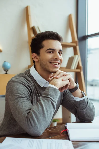 Focus selettivo dell'uomo d'affari con le mani serrate che guarda la fotocamera e sorride a tavola — Foto stock