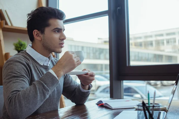 Pensativo empresario sosteniendo platillo y taza de café en la mesa en la oficina - foto de stock