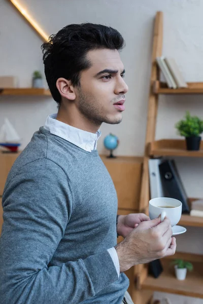 Продуманий бізнесмен тримає тарілку і чашку кави в офісі — стокове фото