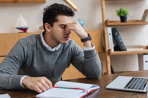 Uomo d'affari stanco con gli occhi chiusi vicino al computer portatile e notebook a tavola in ufficio — Foto stock