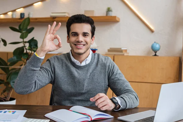 Homme d'affaires regardant la caméra, souriant et montrant un panneau correct à la table dans le bureau — Photo de stock