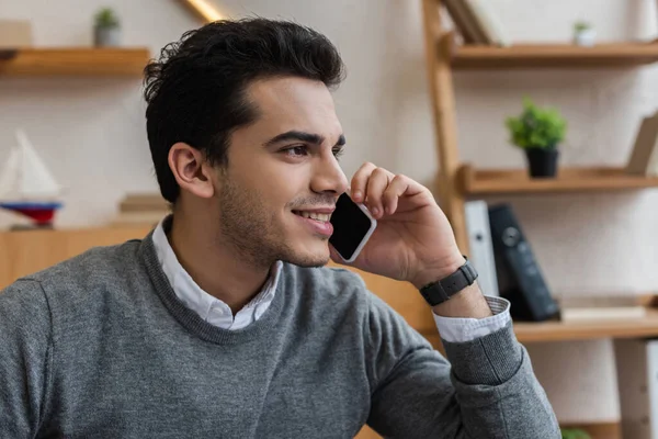 Hombre de negocios sonriendo, mirando hacia otro lado y hablando en el teléfono inteligente en la oficina - foto de stock