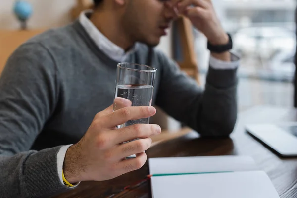 Обрізаний вид бізнесмена з головним болем, що тримає склянку води в офісі — стокове фото