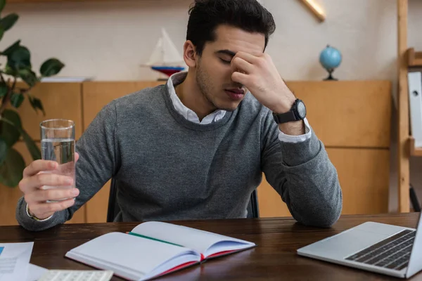 Businessman with glass of water suffering from migraine at table in office — Stock Photo