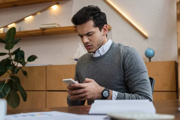 Focus selettivo dell'uomo d'affari preoccupato che chatta sullo smartphone a tavola in ufficio — Foto stock