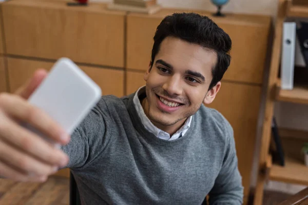 Enfoque selectivo del hombre de negocios sonriendo y tomando selfie en la oficina - foto de stock