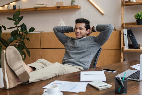 Empresario con las manos detrás de la cabeza poner las piernas en la mesa en la oficina - foto de stock