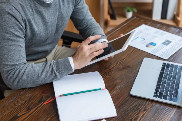 Vista ritagliata di uomo d'affari che lavora con tablet digitale vicino a notebook e laptop a tavola in ufficio — Foto stock