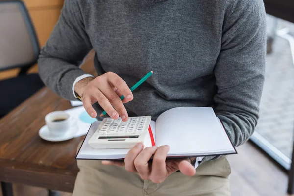 Ausgeschnittene Ansicht eines Geschäftsmannes mit Bleistift und Notizbuch mit Taschenrechner im Büro — Stockfoto