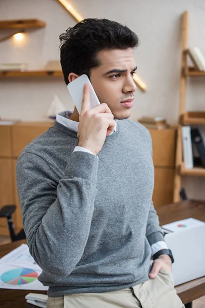 Businessman with hand in pocket talking on smartphone in office — Stock Photo