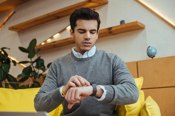 Hombre mirando reloj de pulsera en sofá en la sala de estar - foto de stock