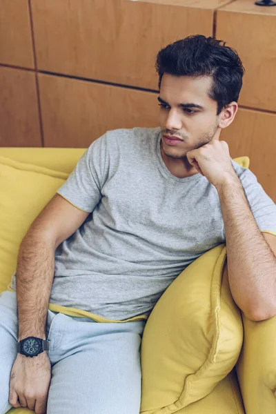 Thoughtful man on yellow sofa in living room — Stock Photo