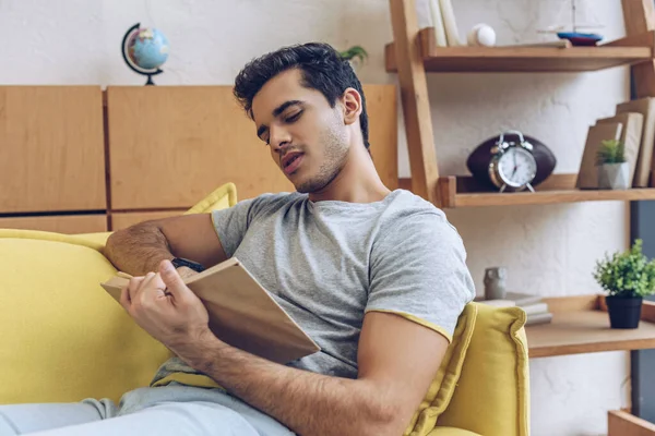 Hombre leyendo libro y acostado en el sofá en la sala de estar - foto de stock