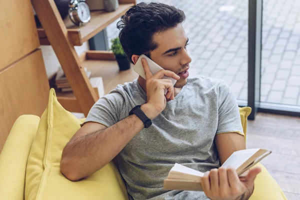 Aus der Vogelperspektive: Mann mit Buch spricht auf Smartphone auf Sofa im Wohnzimmer — Stockfoto