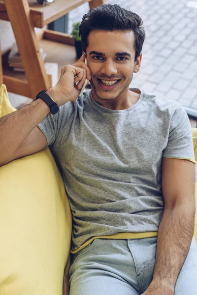 High angle view of man talking on smartphone, looking at camera and smiling on sofa — Stock Photo