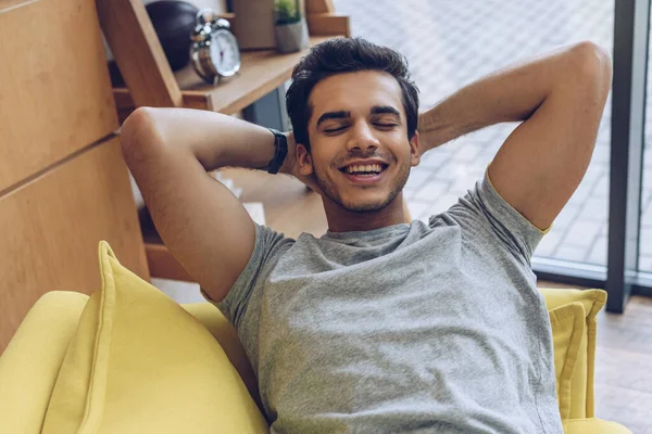 Vista de alto ángulo del hombre con las manos detrás de la cabeza y los ojos cerrados sonriendo en el sofá - foto de stock