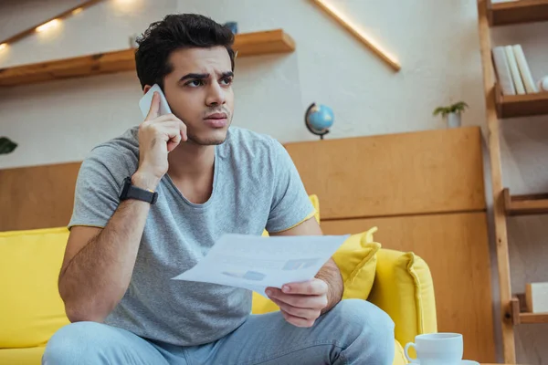 Freelancer talking on smartphone and holding paper on sofa — Stock Photo