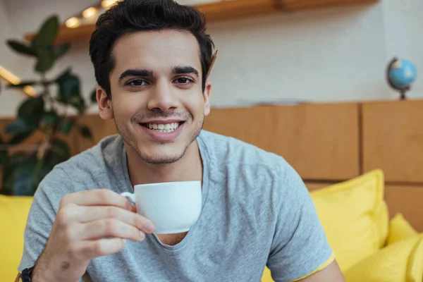 Человек с чашкой кофе улыбается и смотрит в камеру — стоковое фото