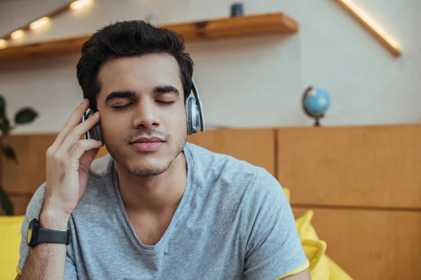 Hombre en auriculares con los ojos cerrados escuchando música en la sala de estar - foto de stock