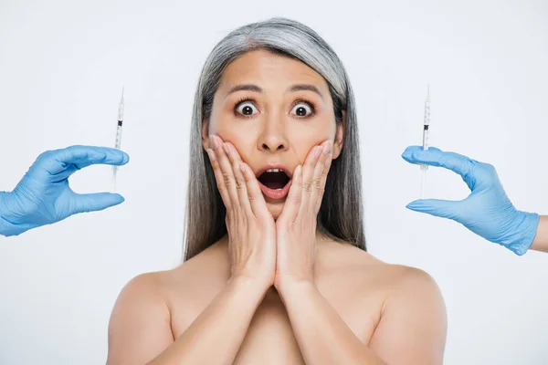 Choqué nu asiatique femme et les médecins en latex gants tenant seringues avec beauté injections isolé sur gris — Photo de stock