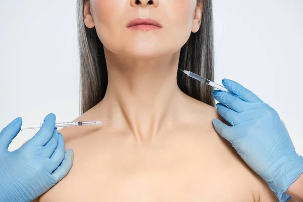 Vista recortada de mujer asiática desnuda y médicos en guantes de látex sosteniendo jeringas con inyecciones de belleza aisladas en gris - foto de stock