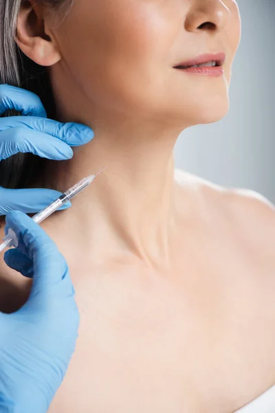 Vue recadrée d'une femme nue souriante et d'un médecin en gants de latex tenant une seringue avec injection de beauté isolée sur du gris — Photo de stock