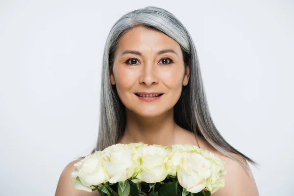 Sonriente mujer asiática desnuda con pelo gris sosteniendo ramo de rosas blancas aisladas en gris - foto de stock