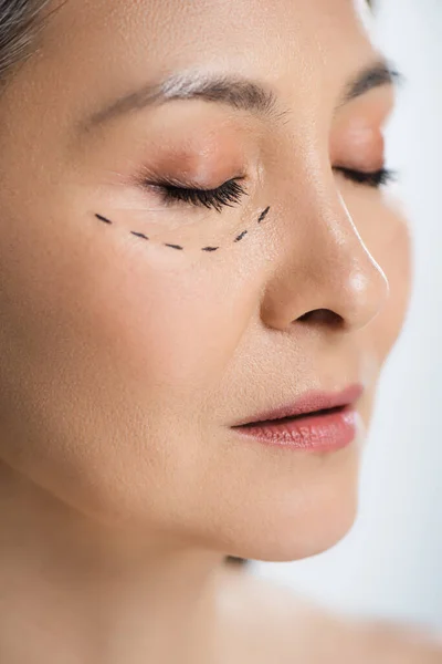 Mujer asiática con los ojos cerrados y líneas de cirugía plástica en la cara aislada en gris - foto de stock