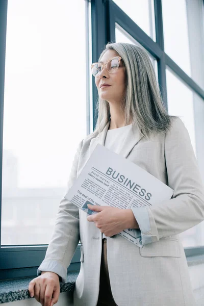 Selbstbewusste asiatische Geschäftsfrau mit Brille hält Wirtschaftszeitung im Amt — Stockfoto