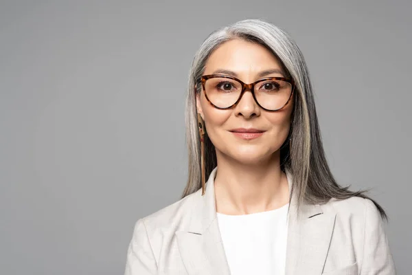 Attractive smiling asian businesswoman in eyeglasses isolated on grey — Stock Photo