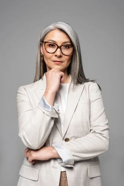 Стомлена азіатська бізнес-леді в окулярах ізольована на сірому — стокове фото