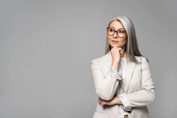 Hermosa reflexivo asiático mujer de negocios en gafas aislado en gris - foto de stock