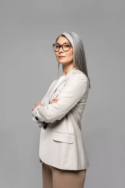 Beautiful asian businesswoman in eyeglasses with crossed arms isolated on grey — Stock Photo