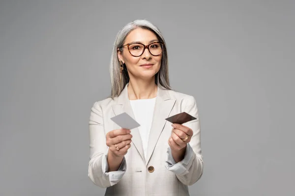 Atractivo asiático mujer de negocios holding tarjetas de visita aislado en gris - foto de stock