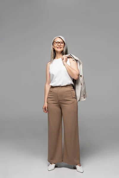 Feliz asiático mujer de negocios en gafas de pie en gris - foto de stock