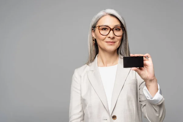 Sonriente asiático mujer de negocios holding tarjeta aislado en gris - foto de stock