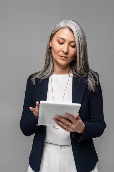 Серйозна азіатська бізнес-леді, використовуючи цифровий планшет ізольовані на сірому — стокове фото