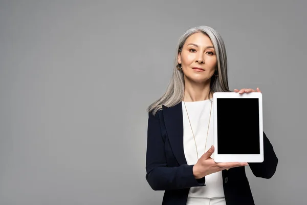 Atractiva mujer de negocios asiática presentando tableta digital con pantalla en blanco aislado en gris - foto de stock