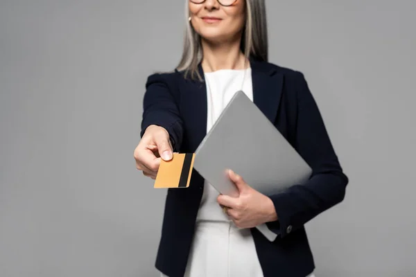 Abgeschnittene Ansicht einer Geschäftsfrau mit grauen Haaren, die online mit Kreditkarte und Laptop einkauft, isoliert auf grau — Stockfoto