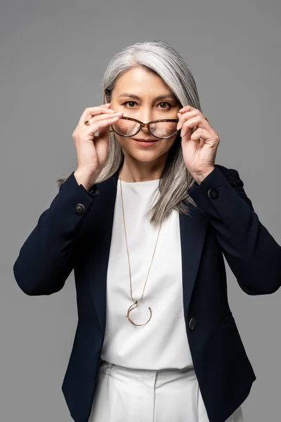 Serious asian businesswoman with grey hair wearing eyeglasses isolated on grey — Stock Photo