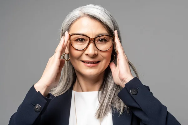 Sonriente asiático mujer de negocios con gris pelo en gafas aislado en gris - foto de stock