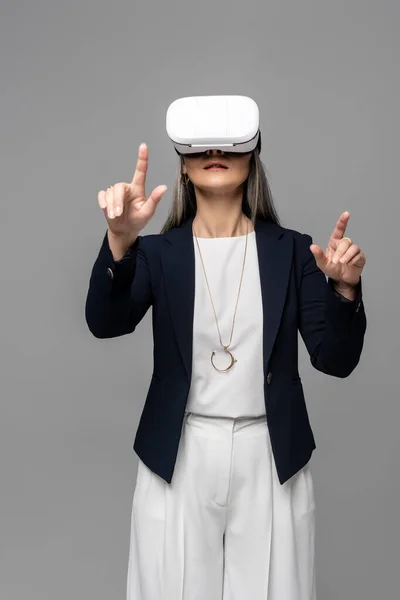 Geschäftsfrau zeigt mit Virtual-Reality-Headset auf grau — Stockfoto