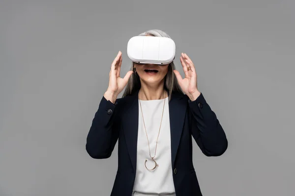 Attractive surprised businesswoman using virtual reality headset isolated on grey — Stock Photo