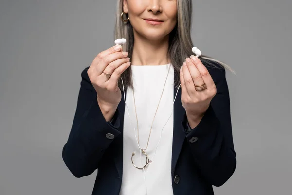 Cropped view of businesswoman with grey hair holding earphones isolated on grey — Stock Photo